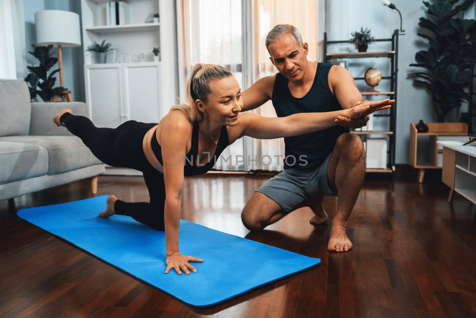 Happy active senior couple in sportswear being supportive and assist on yoga posture together at home. Healthy senior man and woman lifestyle with yoga exercise. Clout