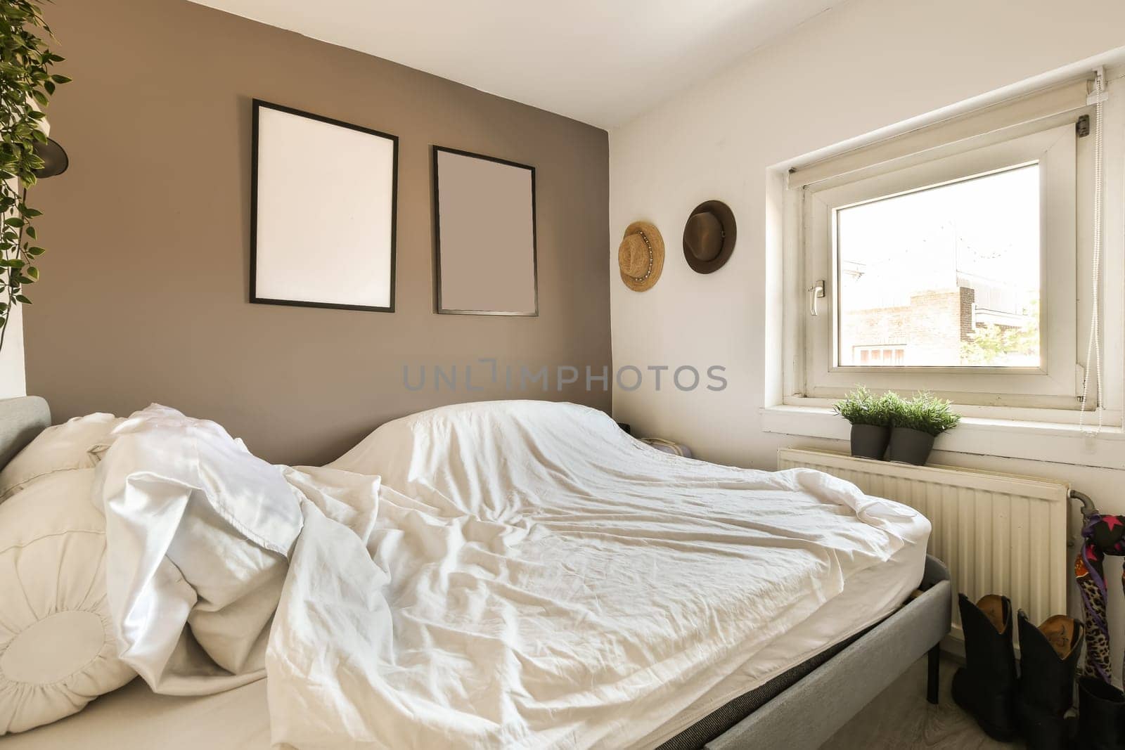 an unmade bed with white sheets and pillows on it in front of a window, next to a plant