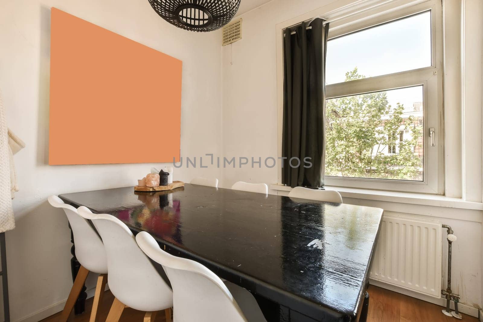 a dining table and chairs in a room with an orange wall art piece on the wall next to the window