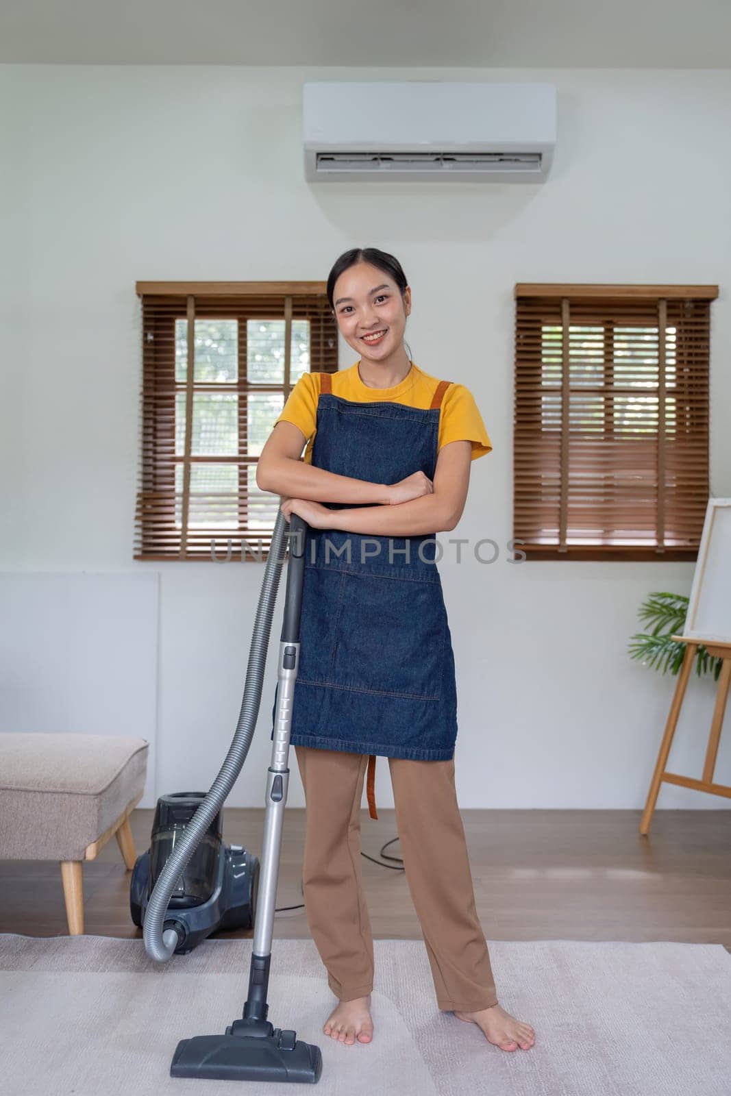 Asian lady doing house chores in apron. young housewife using vacuum clean the floor in the living room by nateemee