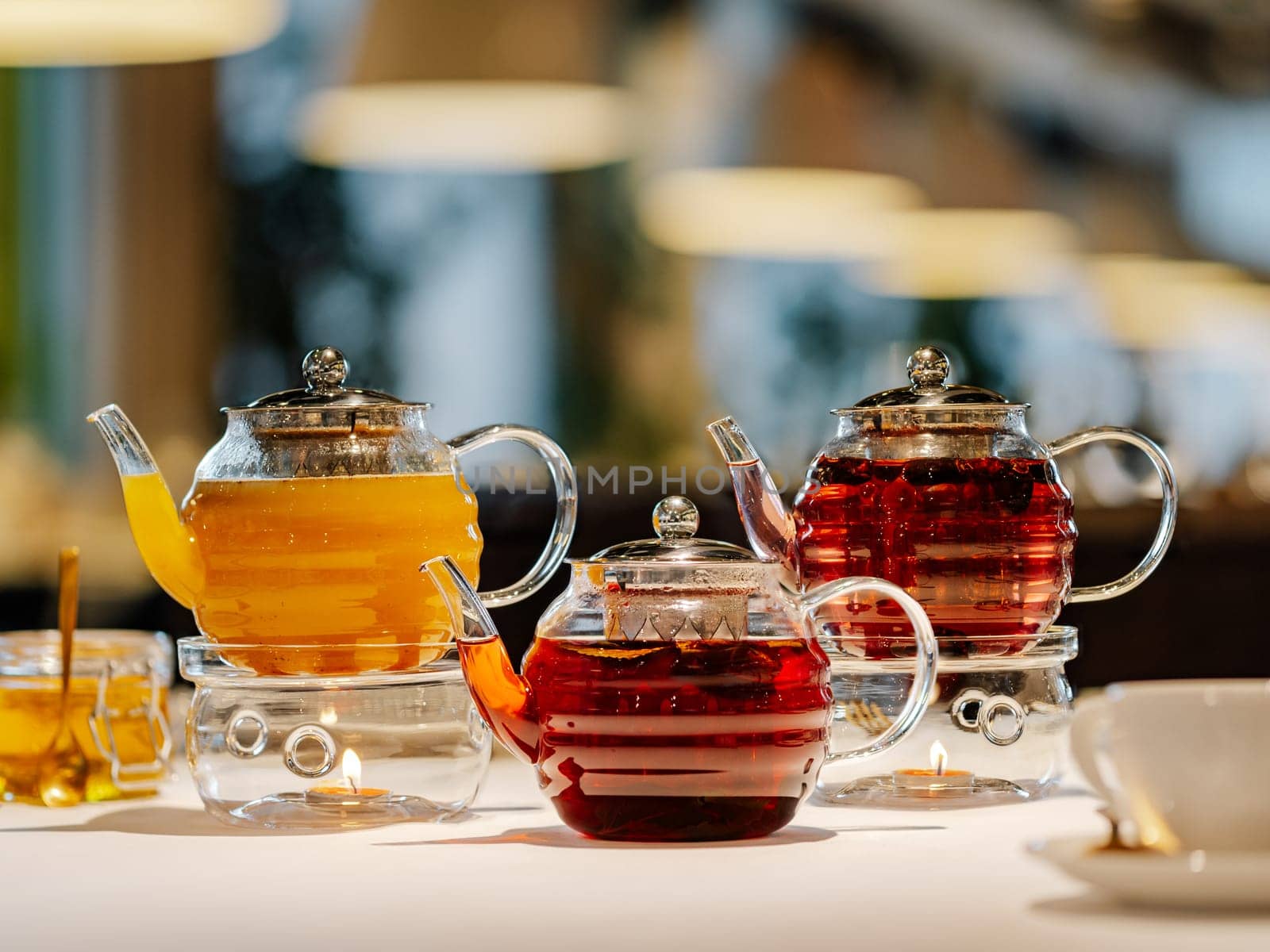 Set of three glass teapots with warmer on table by fascinadora