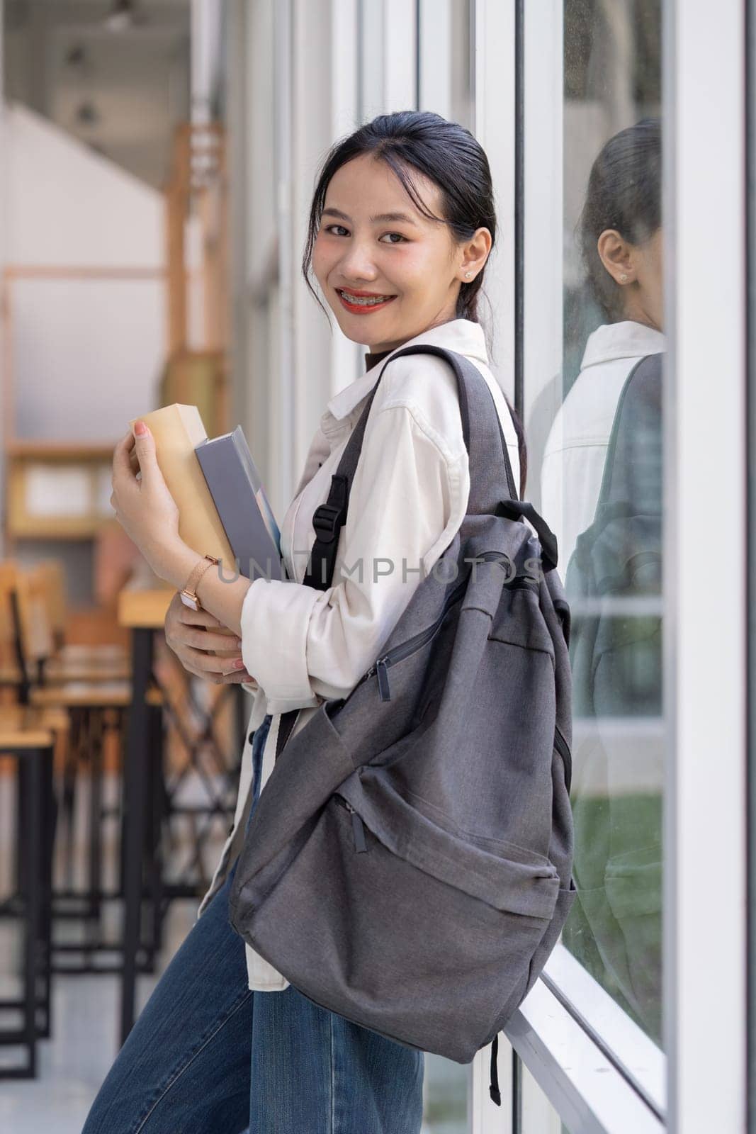 Beautiful young woman asian with backpack and book. College student carrying lots of books in college campus.