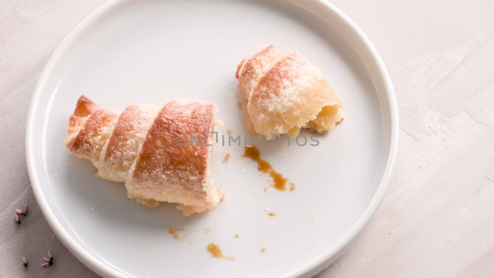 Small croissants in white ceramic plates, homemade cakes on concrete table top.