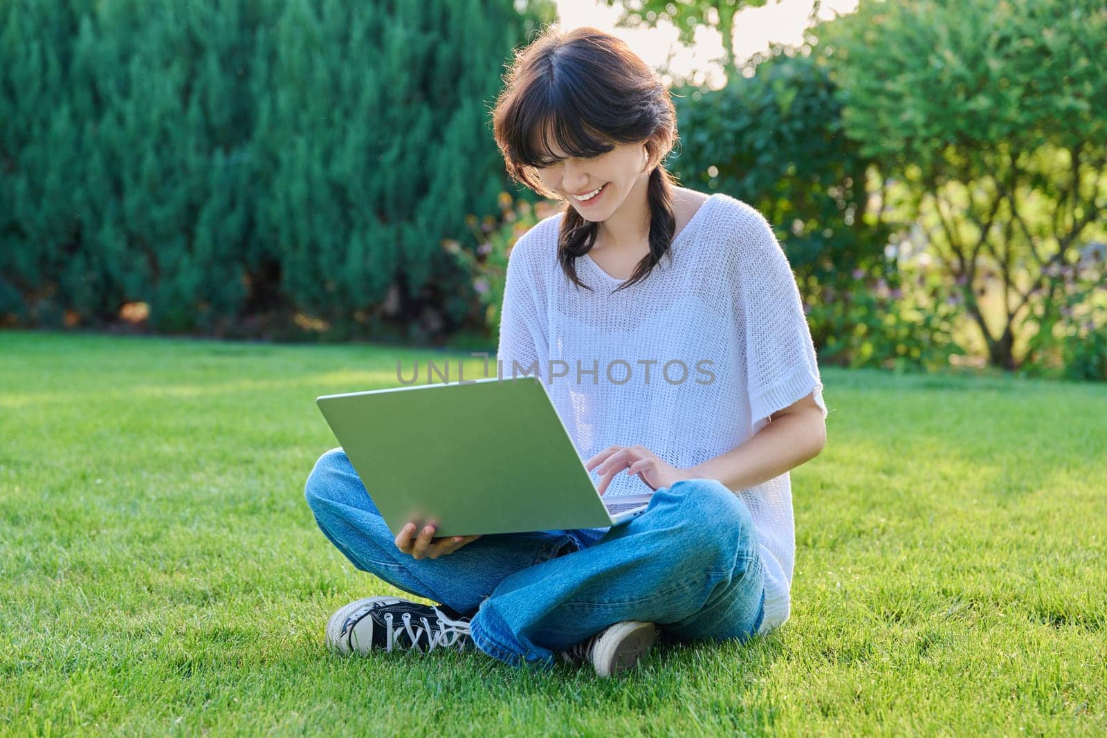 Teenage girl sitting on the grass using a laptop. Female teenager student 18, 19 years old sitting on the lawn, technologies for studying leisure communication shopping in backyard in garden