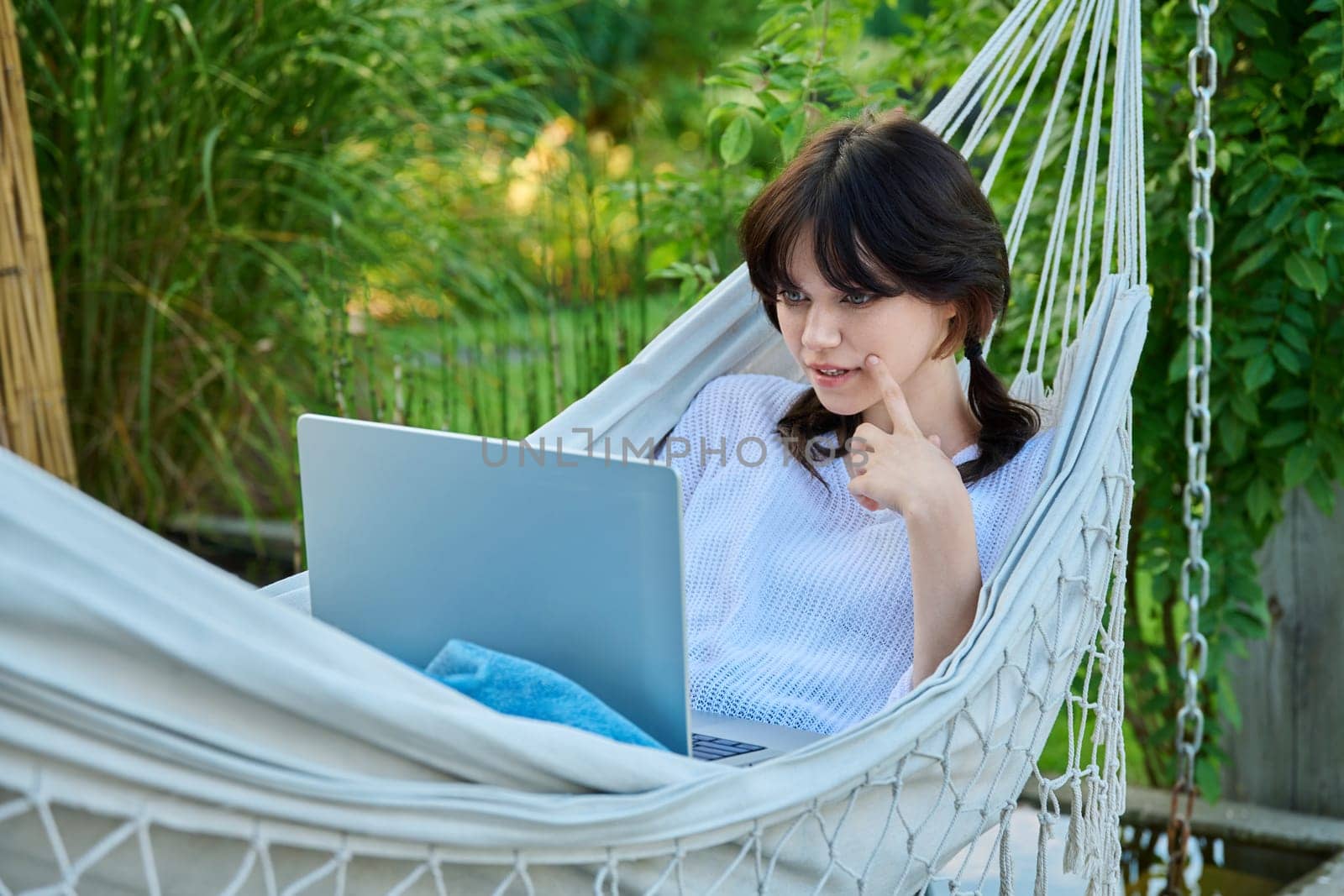 Teenage girl relaxing in hammock using laptop for leisure study. Adolescence, students, high school, technology, lifestyle, youth concept