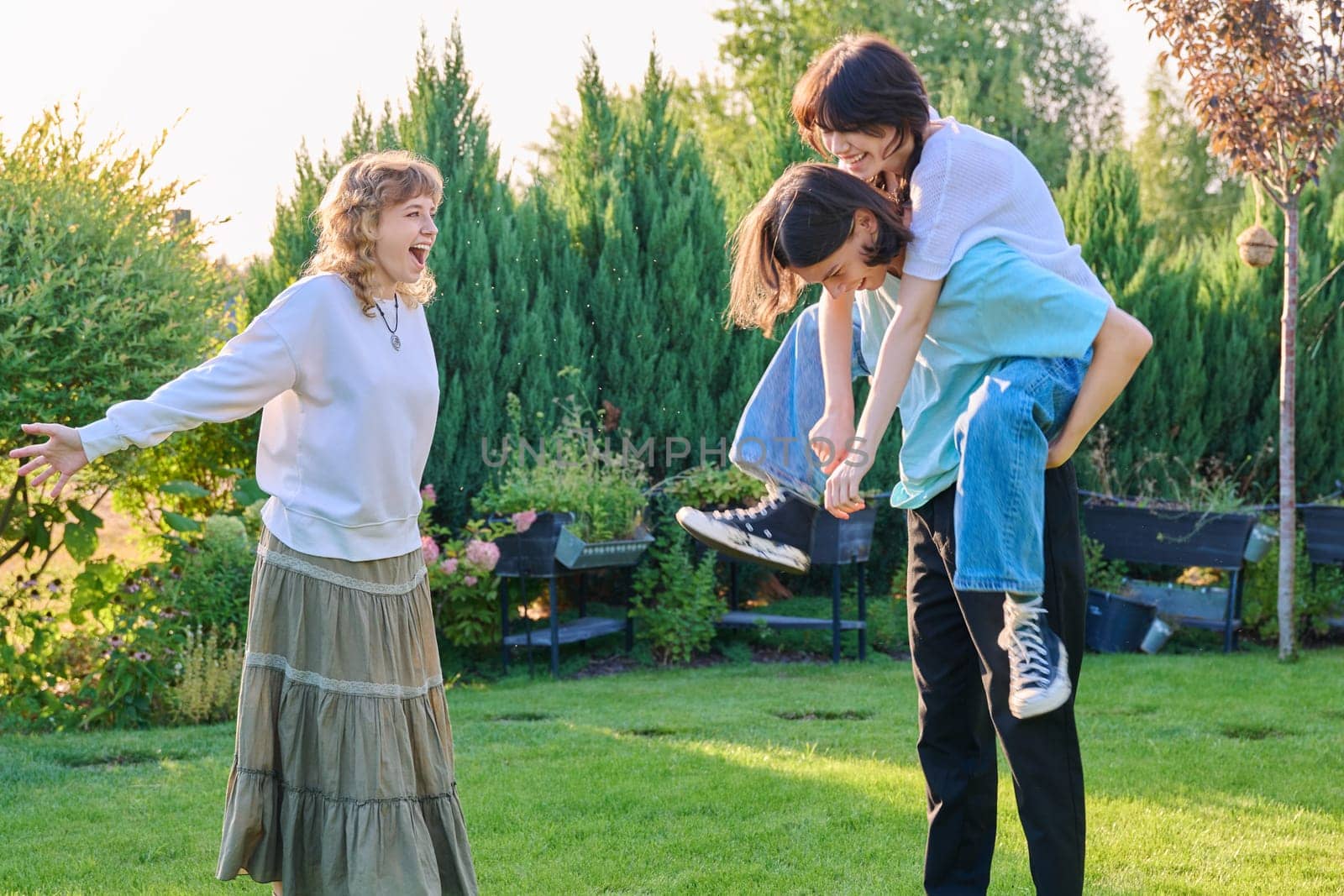 Three teenage friends having fun outdoor, sunny summer day on the lawn. Group of teenagers laughing together. Lifestyle, leisure, friendship, youth concept