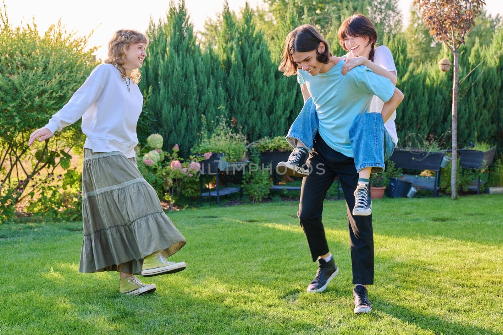 Three teenage friends having fun outdoor, sunny summer day on the lawn. Group of teenagers laughing together. Lifestyle, leisure, friendship, youth concept