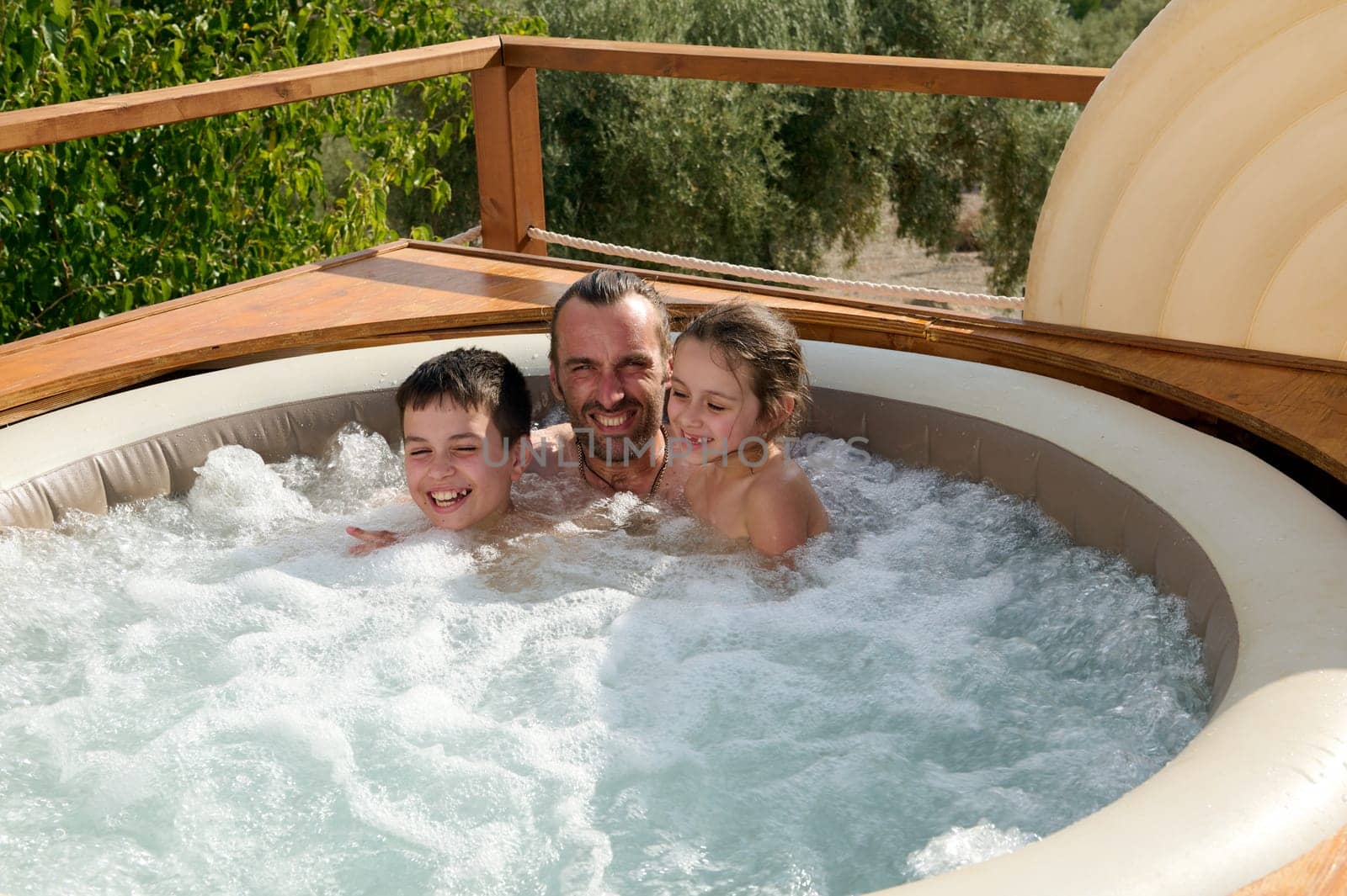 Cheerful loving father hugs his kids, having fun together in outdoor swimming pool, smiling looking at camera. by artgf