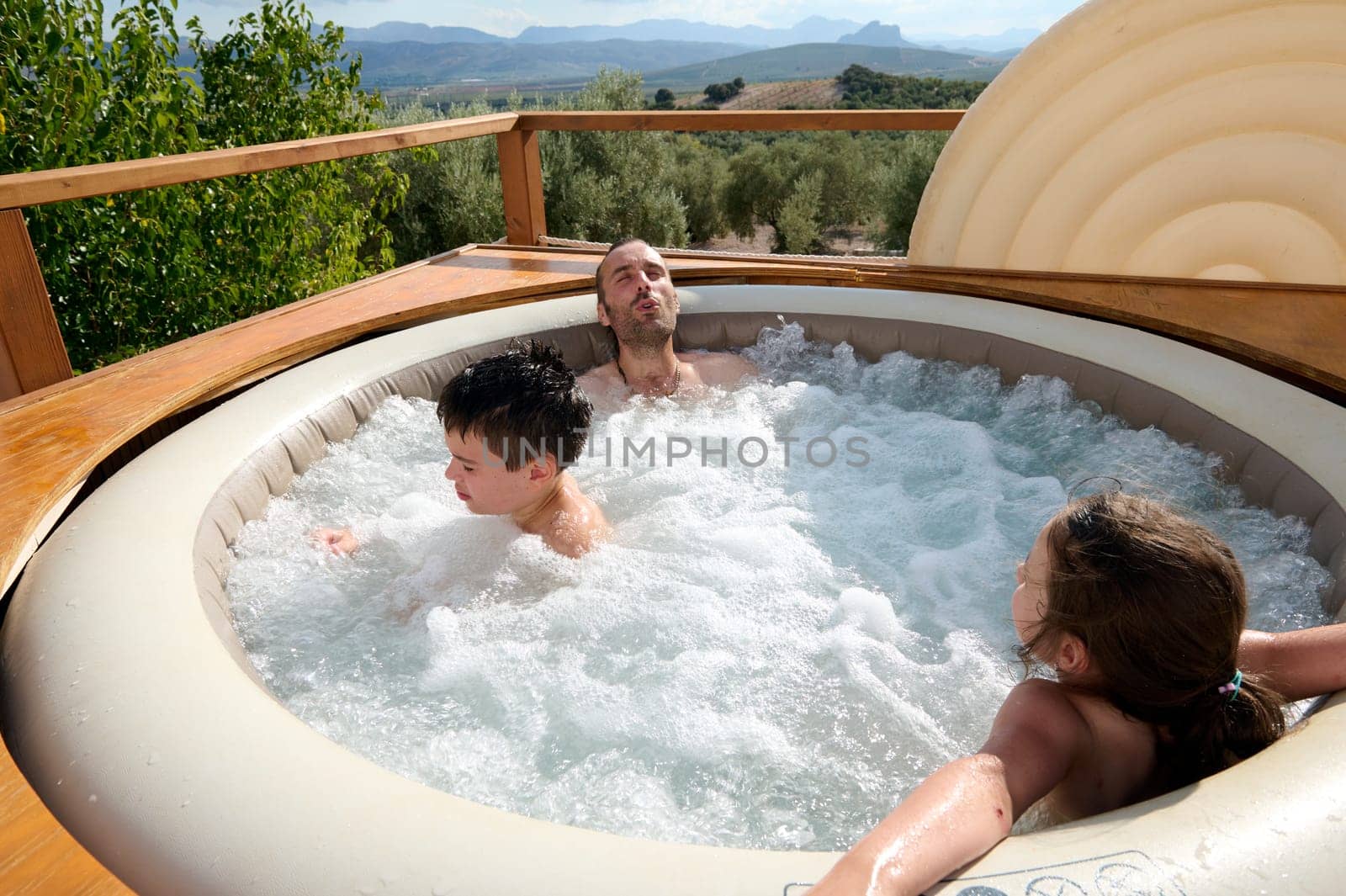 Young adult dad enjoying a weekend with his son and daughter in the swimming pool on a hot sunny summer day. Happy carefree childhood. Family relationships. Summer holidays. People. Leisure activity