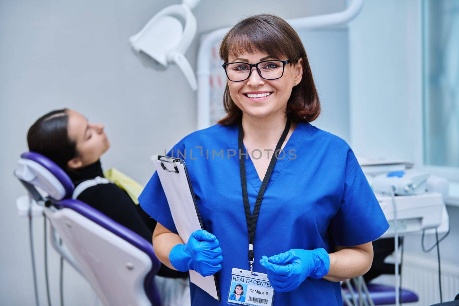 Portrait of smiling female dentist looking at camera with young girl patient sitting in dental chair. Visit to dentist examination treatment. Dentistry hygiene dental teeth health care concept