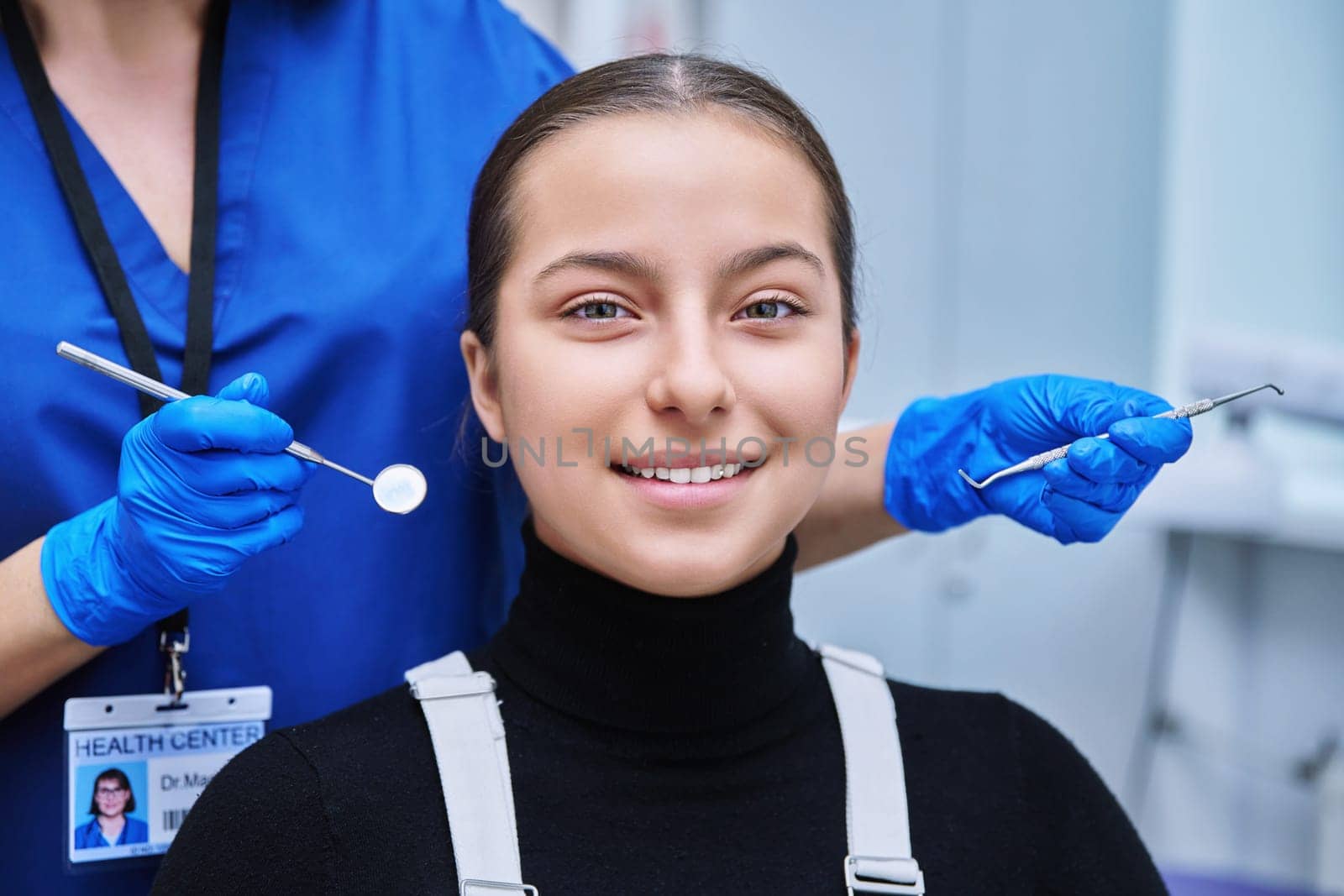 Young teenage female at dental examination treatment checkup in clinic. Teen girl sitting in chair doctor dentist with tools examining patient teeth. Adolescence hygiene dentistry dental health care