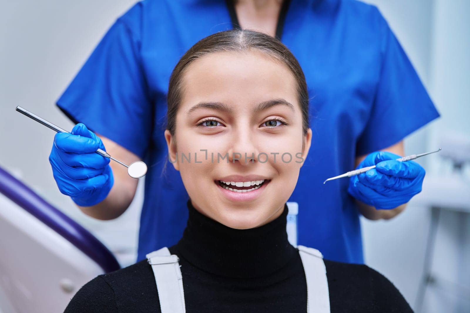 Young teenage female at dental examination treatment checkup in clinic. Teen girl sitting in chair doctor dentist with tools examining patient teeth. Adolescence hygiene dentistry dental health care