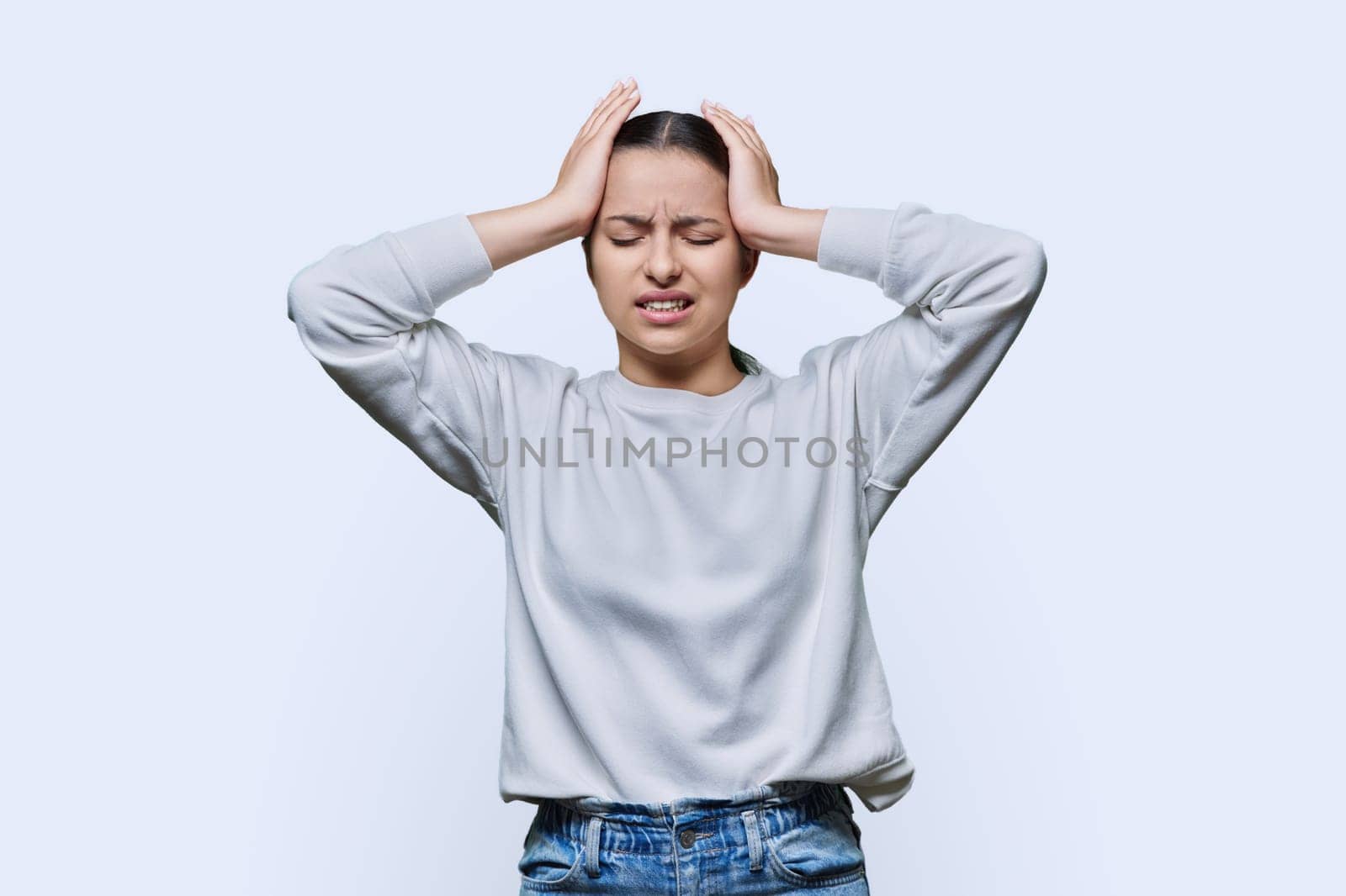 Shocked anxious young woman in panic holding her hands behind her head with her mouth open on white studio background. Teenage student with glasses in hysterics, shock stress helplessness anxiety