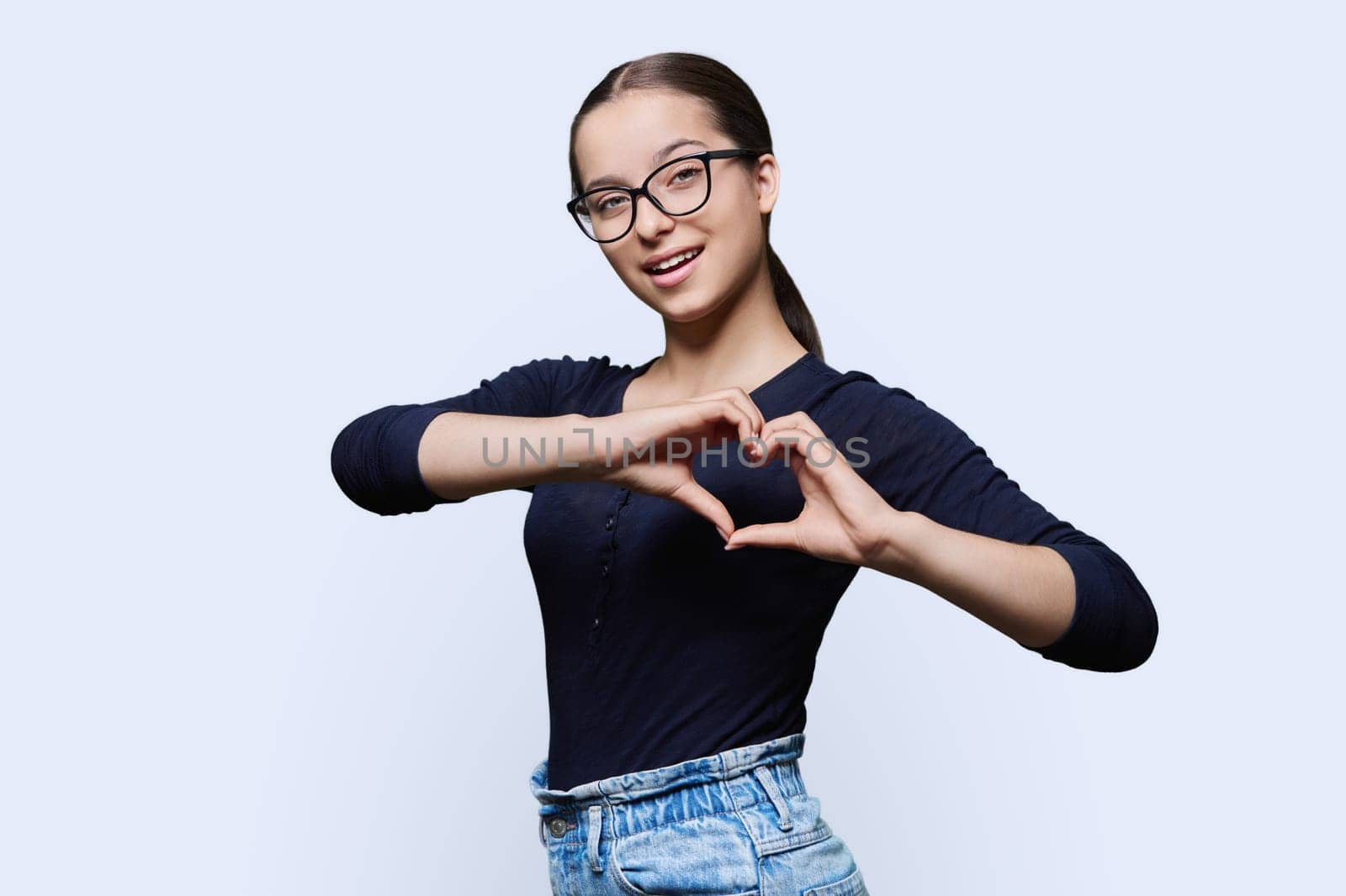 Young smiling female showing heart gesture with fingers, happy female showing love, white studio background. Body language, signs symbols, love, emotions, romance youth concept