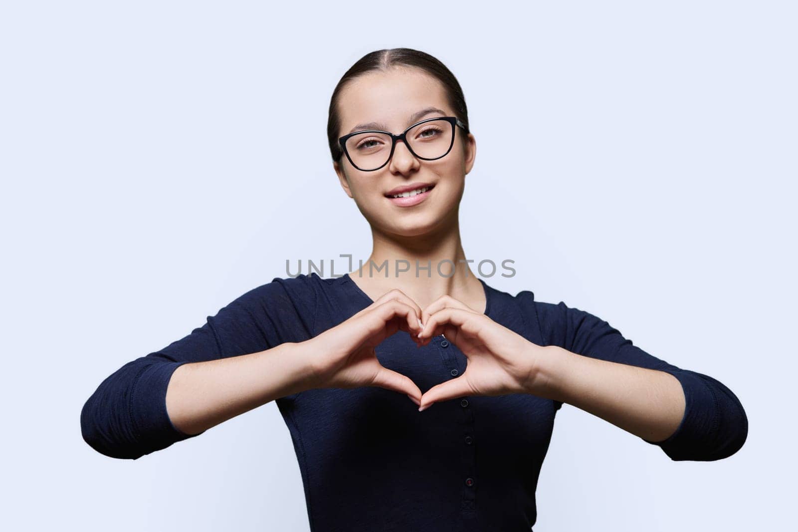 Young smiling female showing heart gesture with fingers, white background by VH-studio