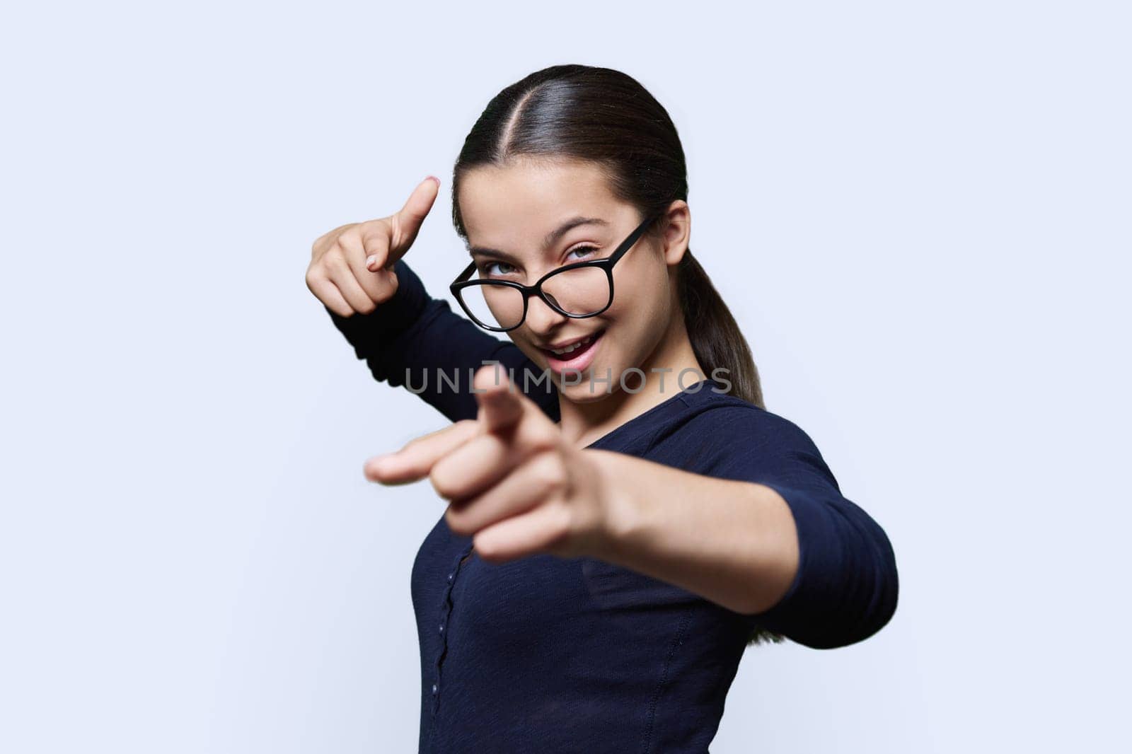 Teenage student girl in glasses looking at camera pointing finger at you, on white studio background. Announcement, highlighting, attention, education, lifestyle people concept
