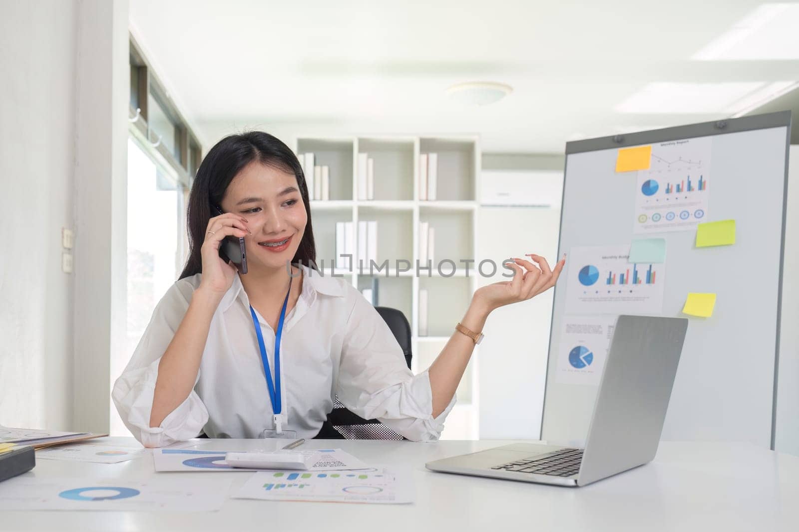 Businesswoman talking on the phone talking with customers and using laptop to do financial management and calculations on white table in office.