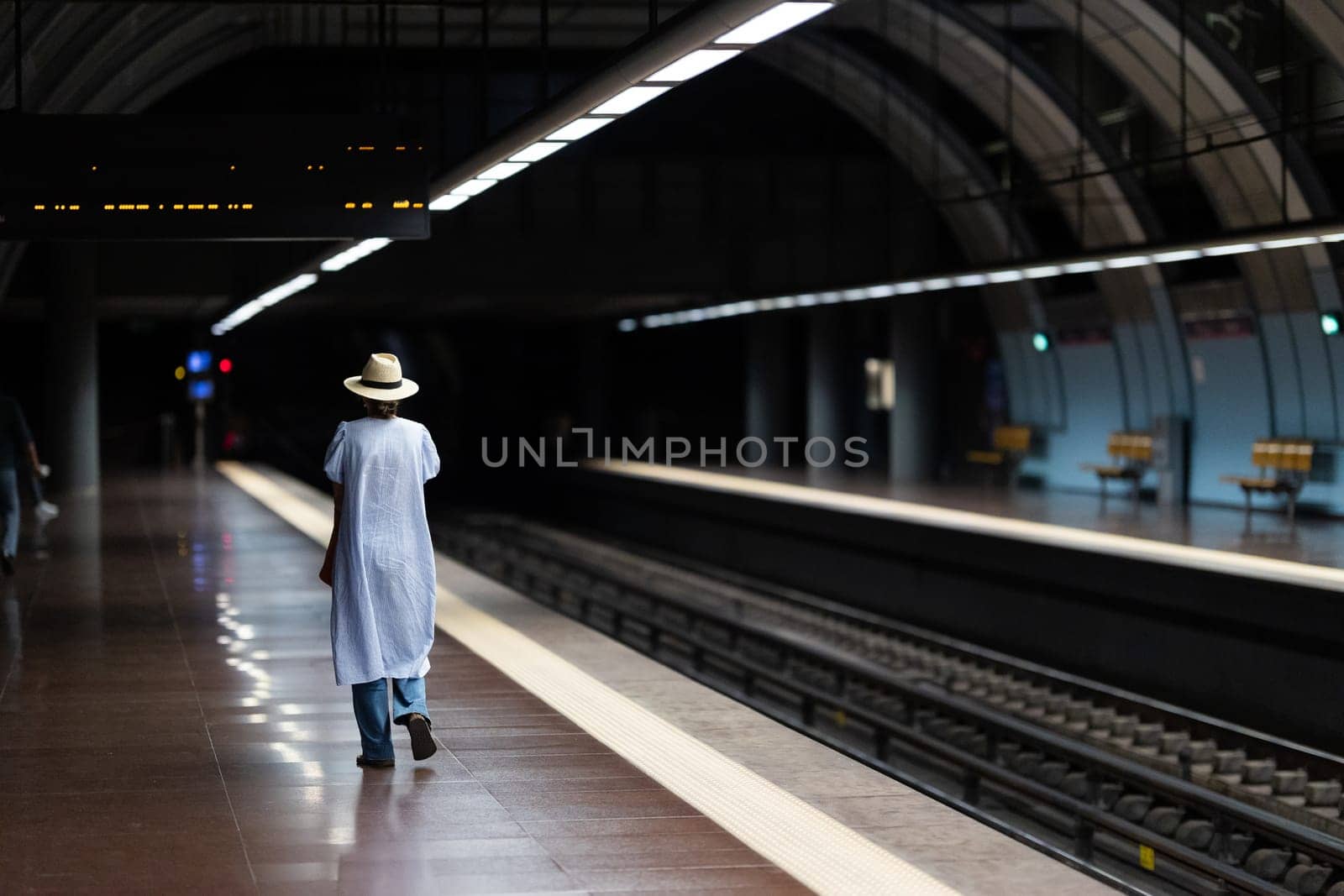 A solitary woman patiently waiting on a well-lit subway platform for the arriving train.
