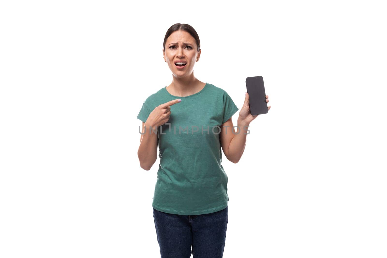 a young charismatic black-haired woman with gathered hair is dressed in a basic t-shirt and jeans, pointing her finger at the smartphone screen in surprise.