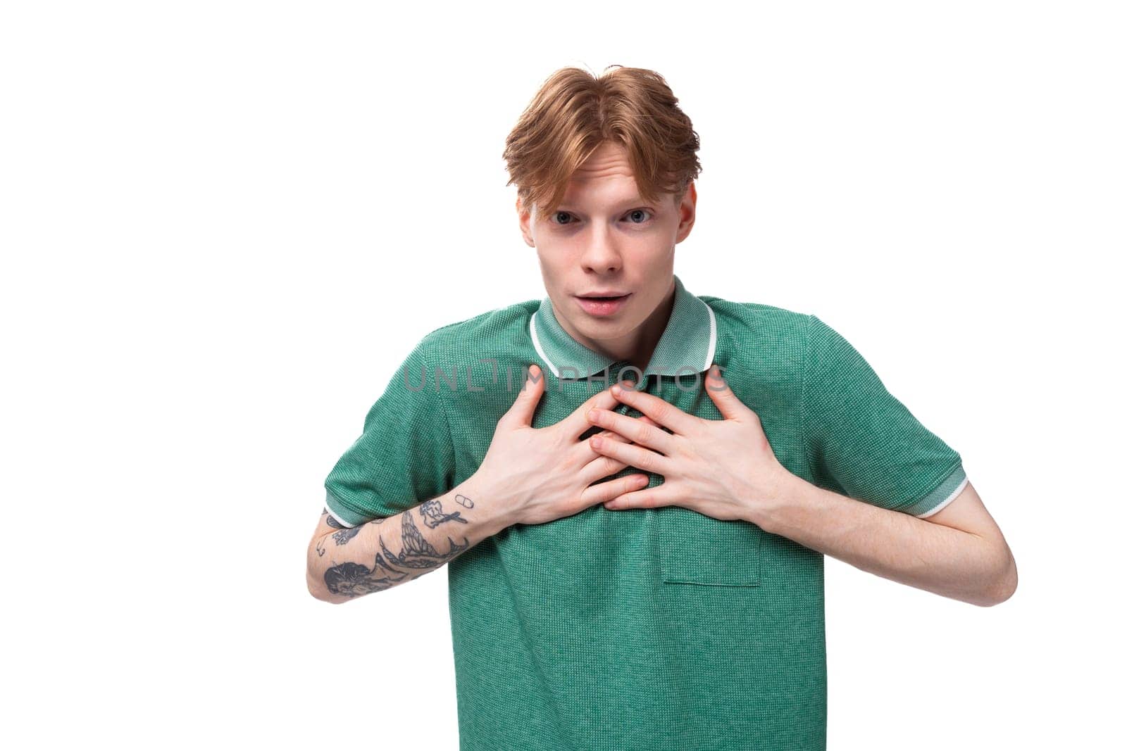 young surprised ginger man with a tattoo on his arm dressed in a green short sleeve t-shirt is shocked.