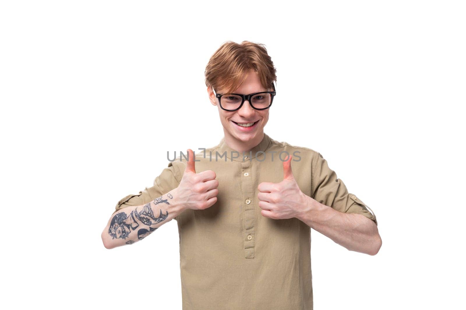 young cheerful optimist handsome man with copper hair with a tattoo on his arm is dressed in a khaki shirt by TRMK