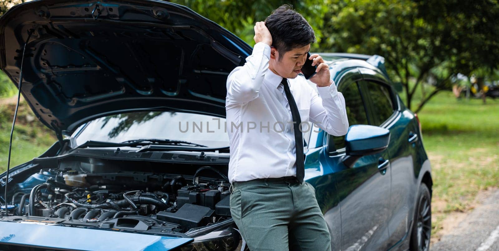 Elegant businessman standing on highway at dusk, waiting for towing service. Horizontal photo of middle-aged man in suit looking lost and contemplative. Concept for transportation problems and journey