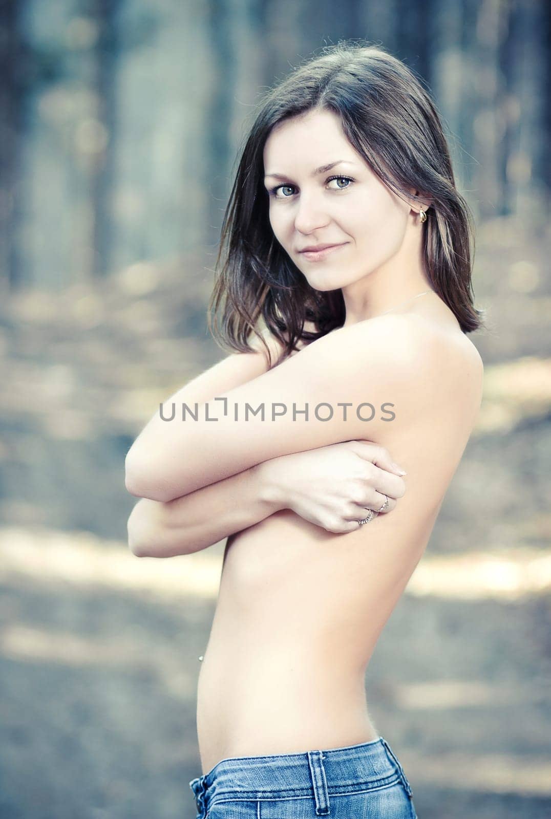 Topless young woman hiding her naked chests under her arms  in a forest.
