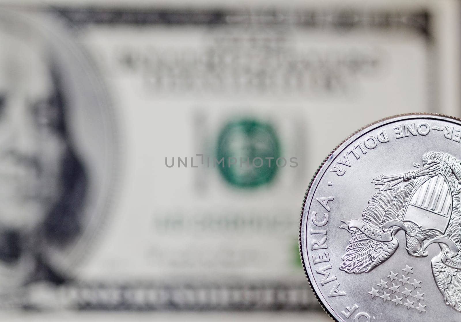 Silver shiny dollar coin on a background of blurry one hundred dollar bill