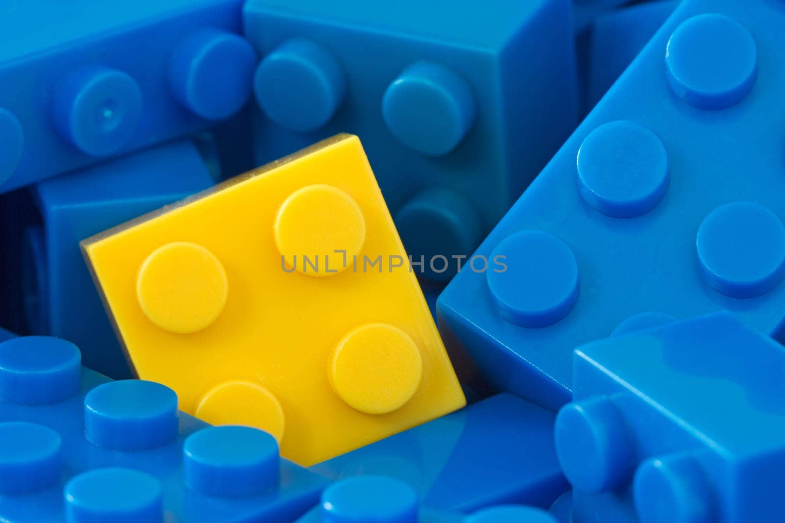 color toy background. yellow plastic brick in a middle of blue ones