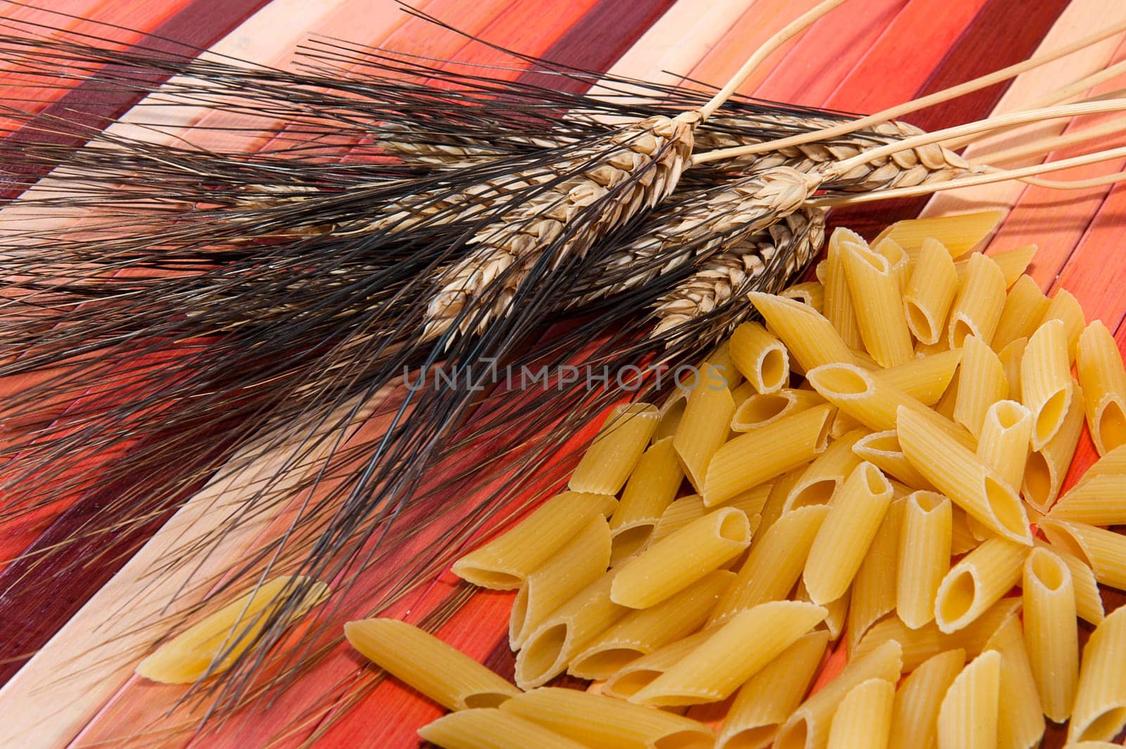 Pasta and ears of wheat colored bamboo background