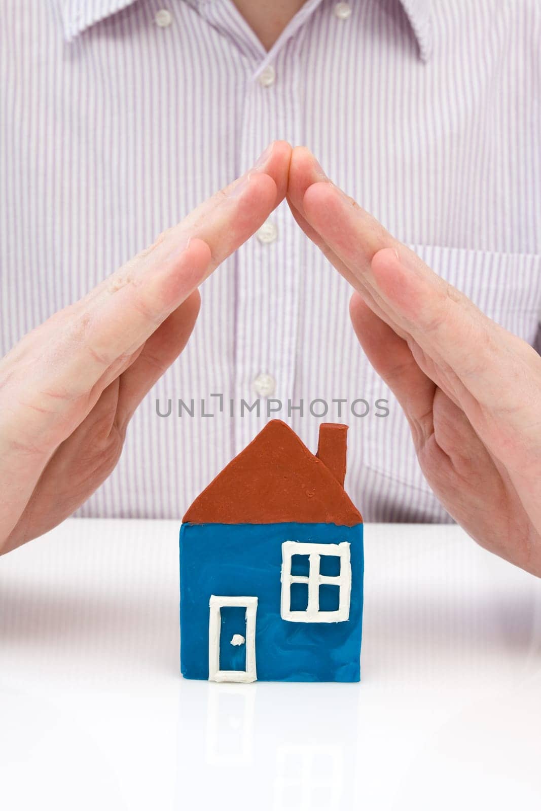 human hands covering house made from plasticine
