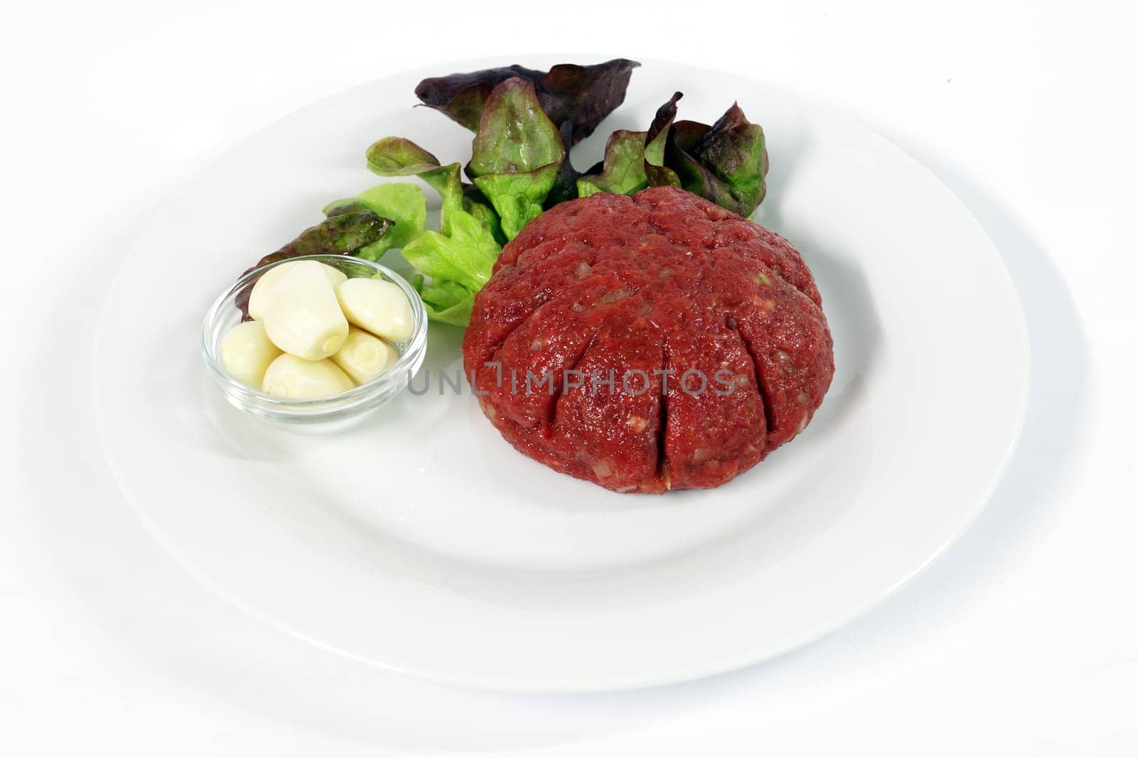 Steak tartare with garlic on white plate with onions and ketchup.