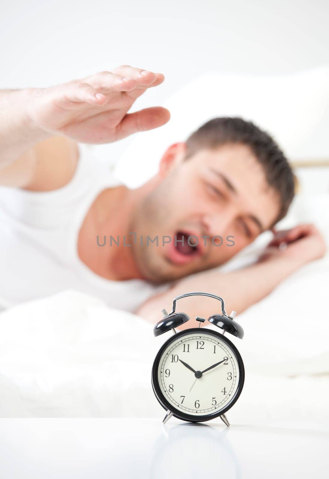 Sleeping man being awakened by an alarm clock