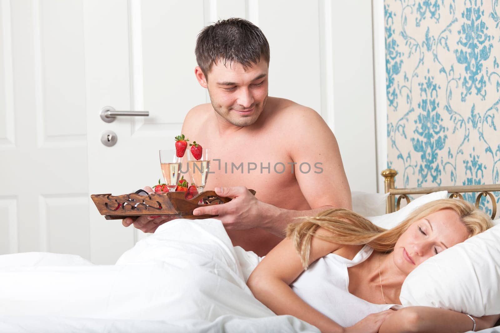 man serving breakfast to bed with two glasses sparkling wine