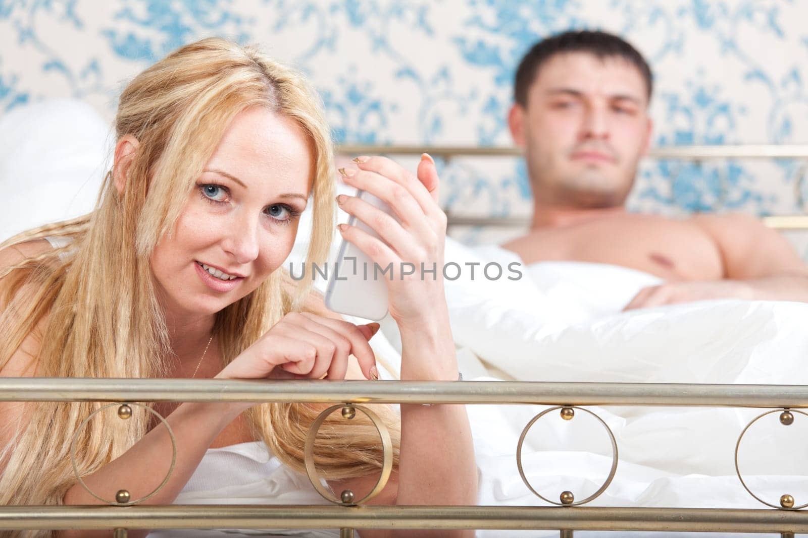 woman with phone on bed and sad man in background