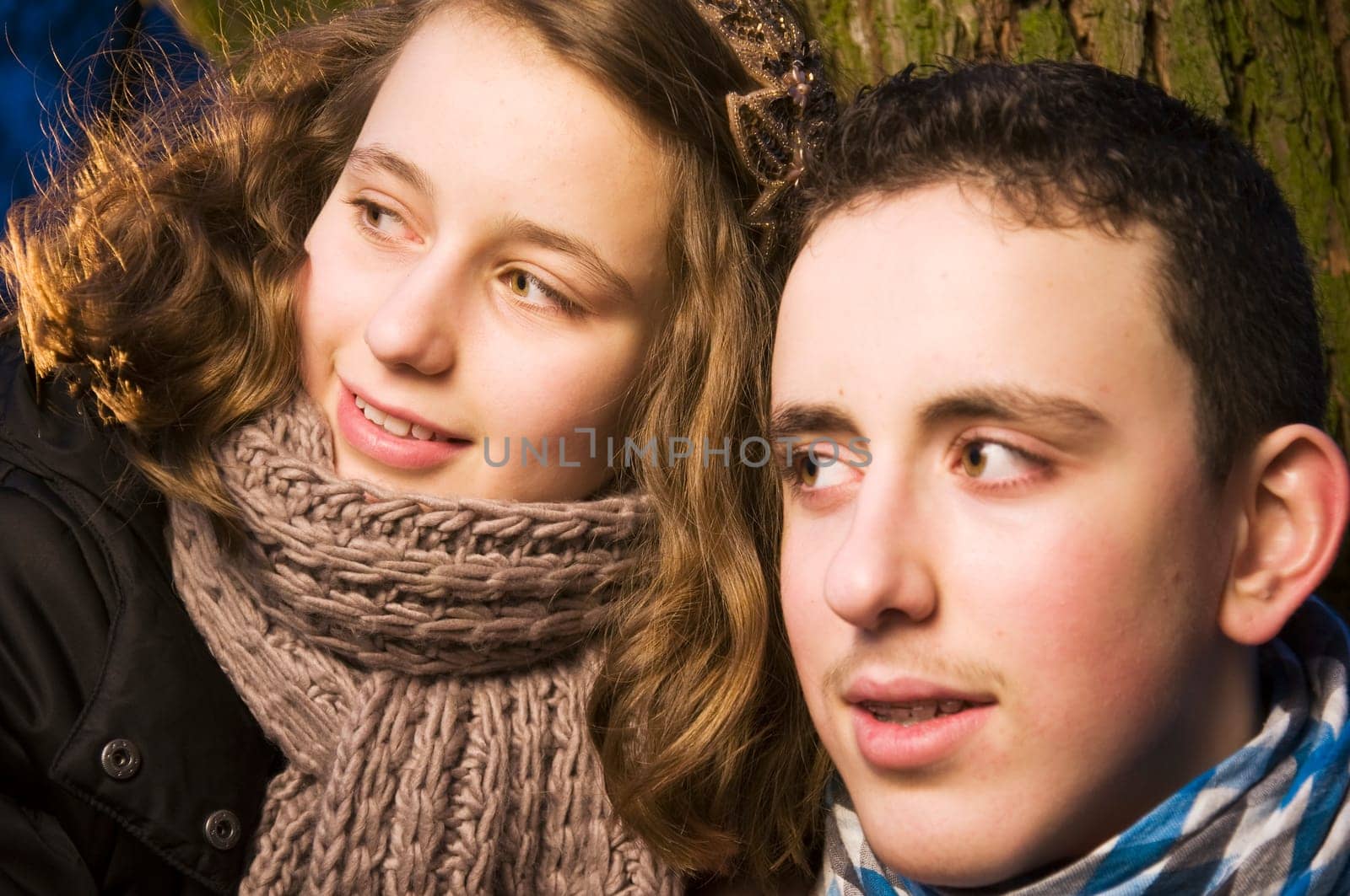 Head and shoulders portraits of two young teenage siblings (brother and sister) laughing at dusk standing by a tree