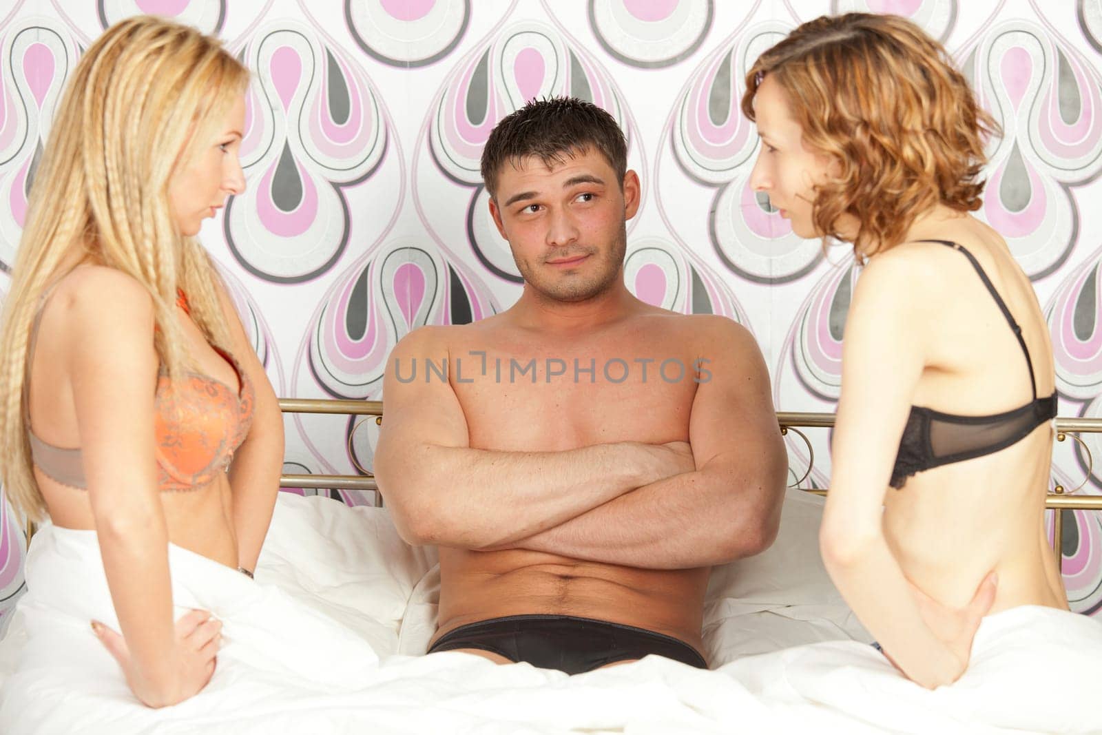 man sitting between two frustrated women in bed - focus on man