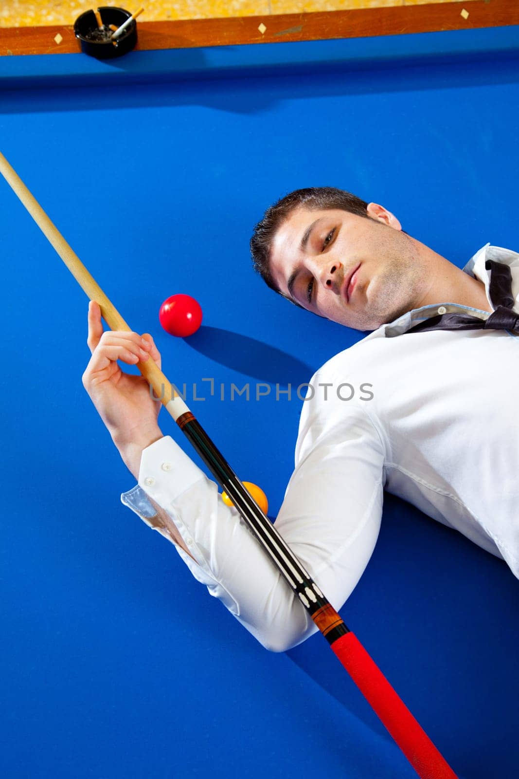 billiard young man player lying on pool blue table with balls