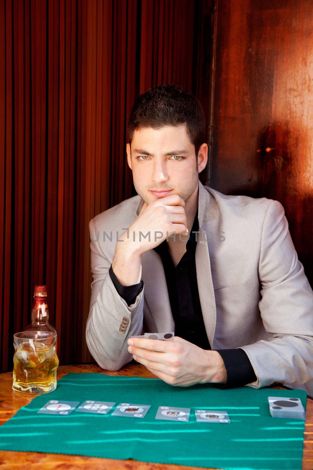 Latin handsome gambler man in table playing poker cards and drinking whisky