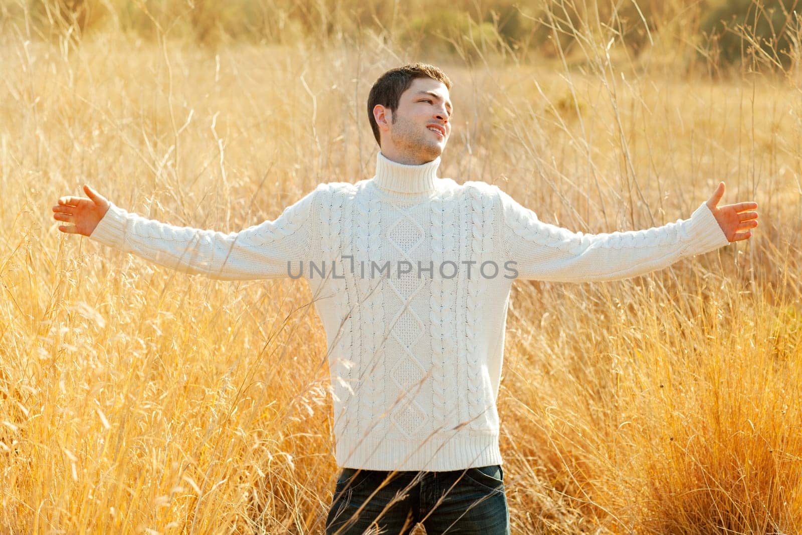 Autumn winter man in outdoor golden grass field with turtleneck sweater open arms