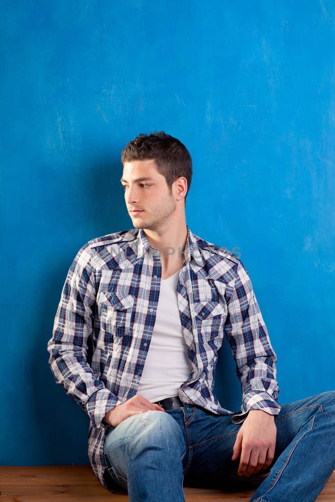 handsome young man with plaid shirt sitting on wood in blue background