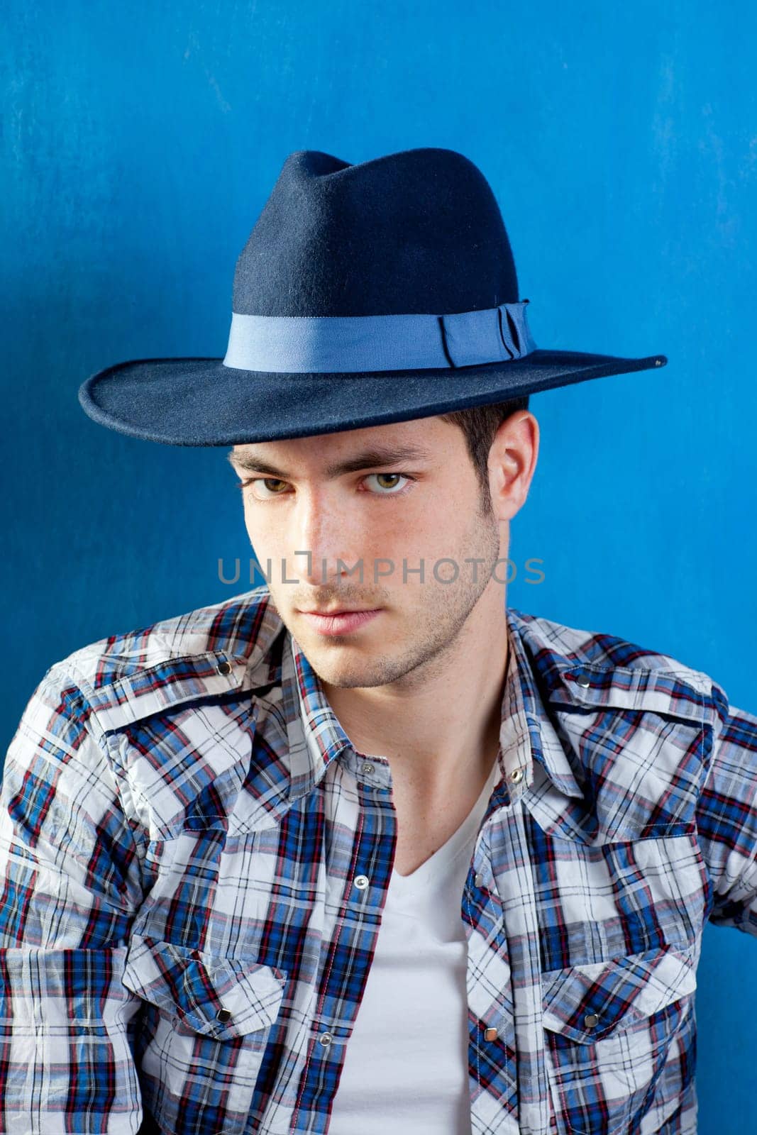 handsome young man with plaid shirt and cowboy hat on blue background