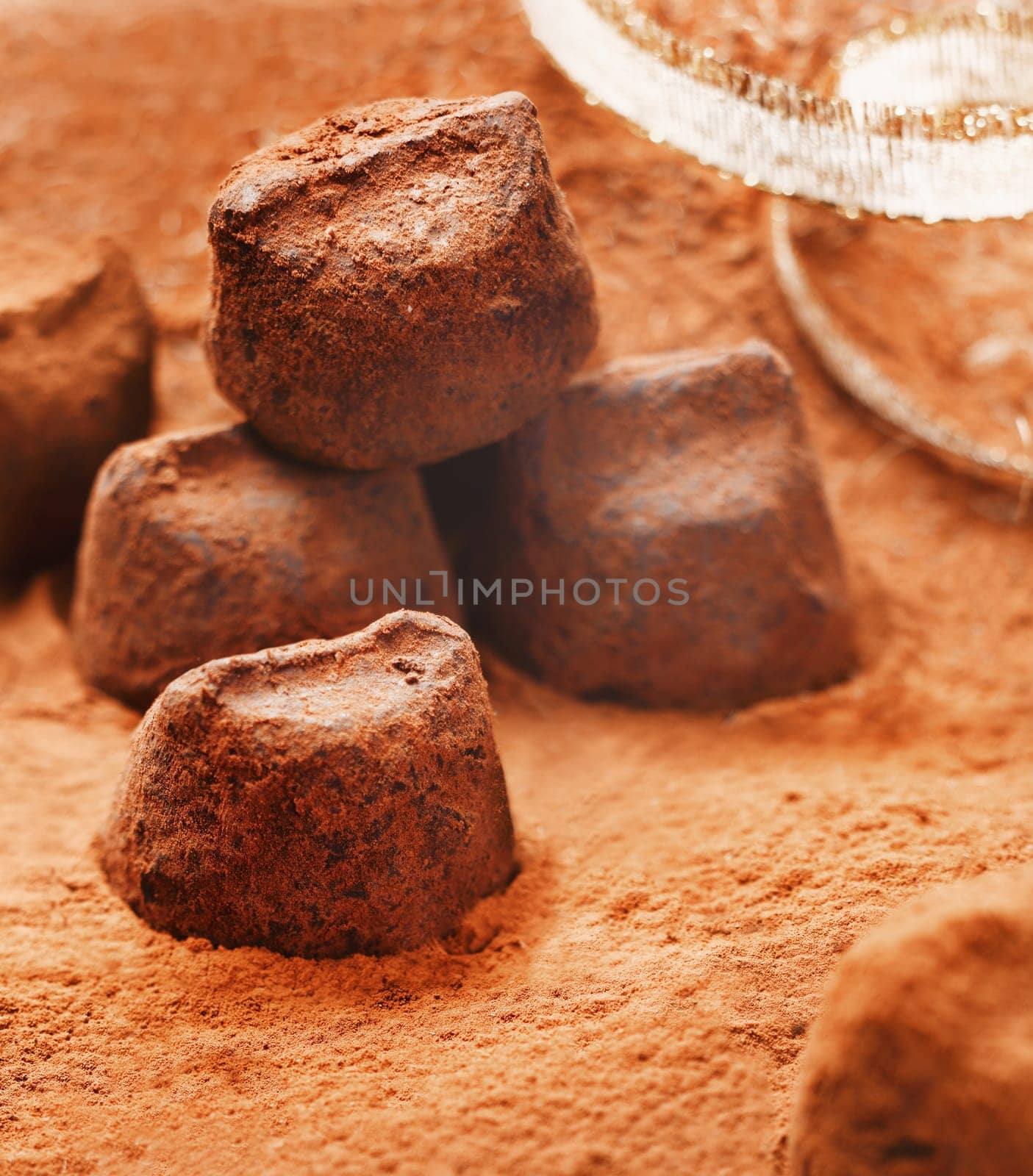Handmade luxury chocolate bonbons sprinkled with, and lying in, cocoa powder with gold festive ribbon