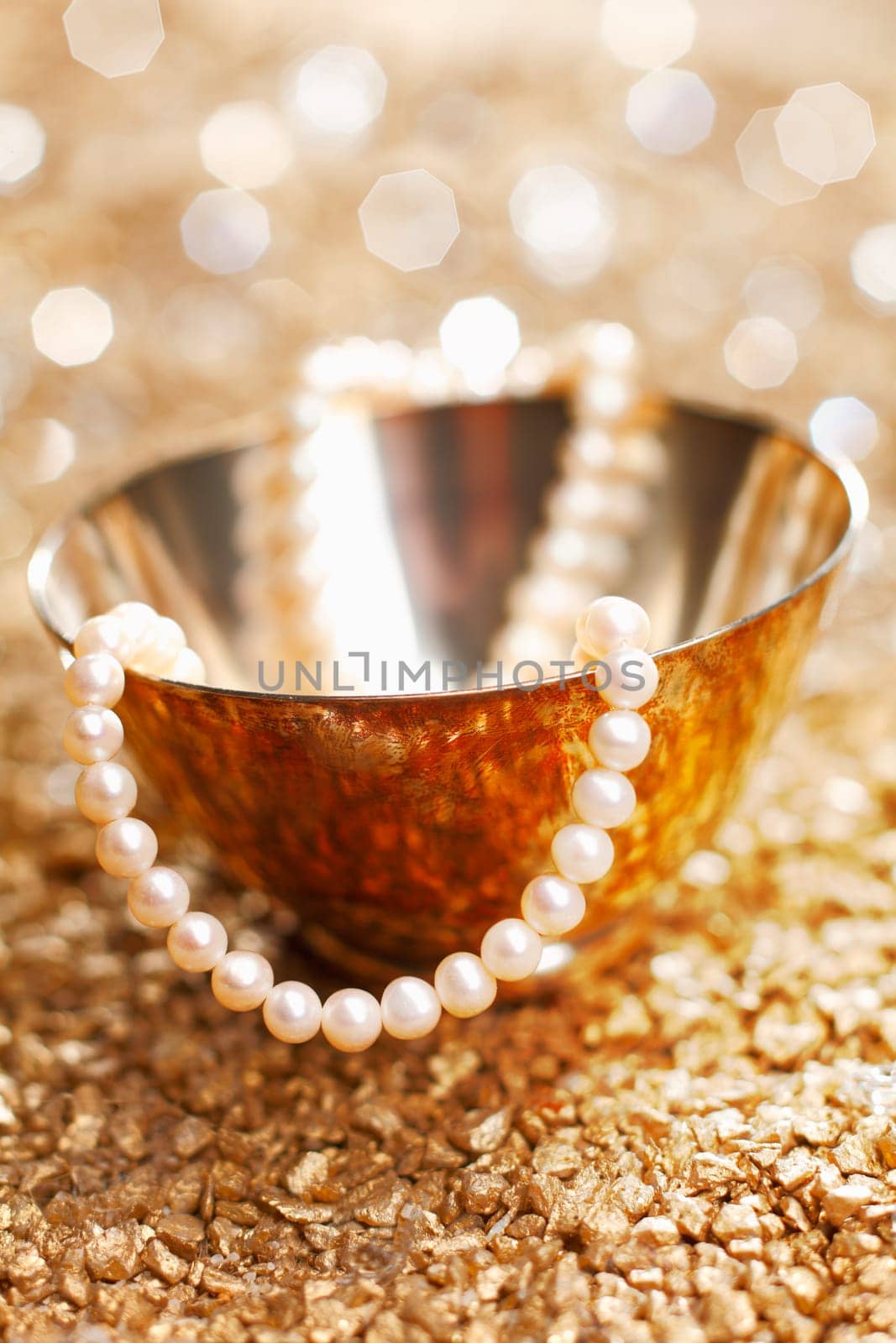 A matched string of pearls cascades down from a pretty silver bowl backed by a bokeh of festive party lights
