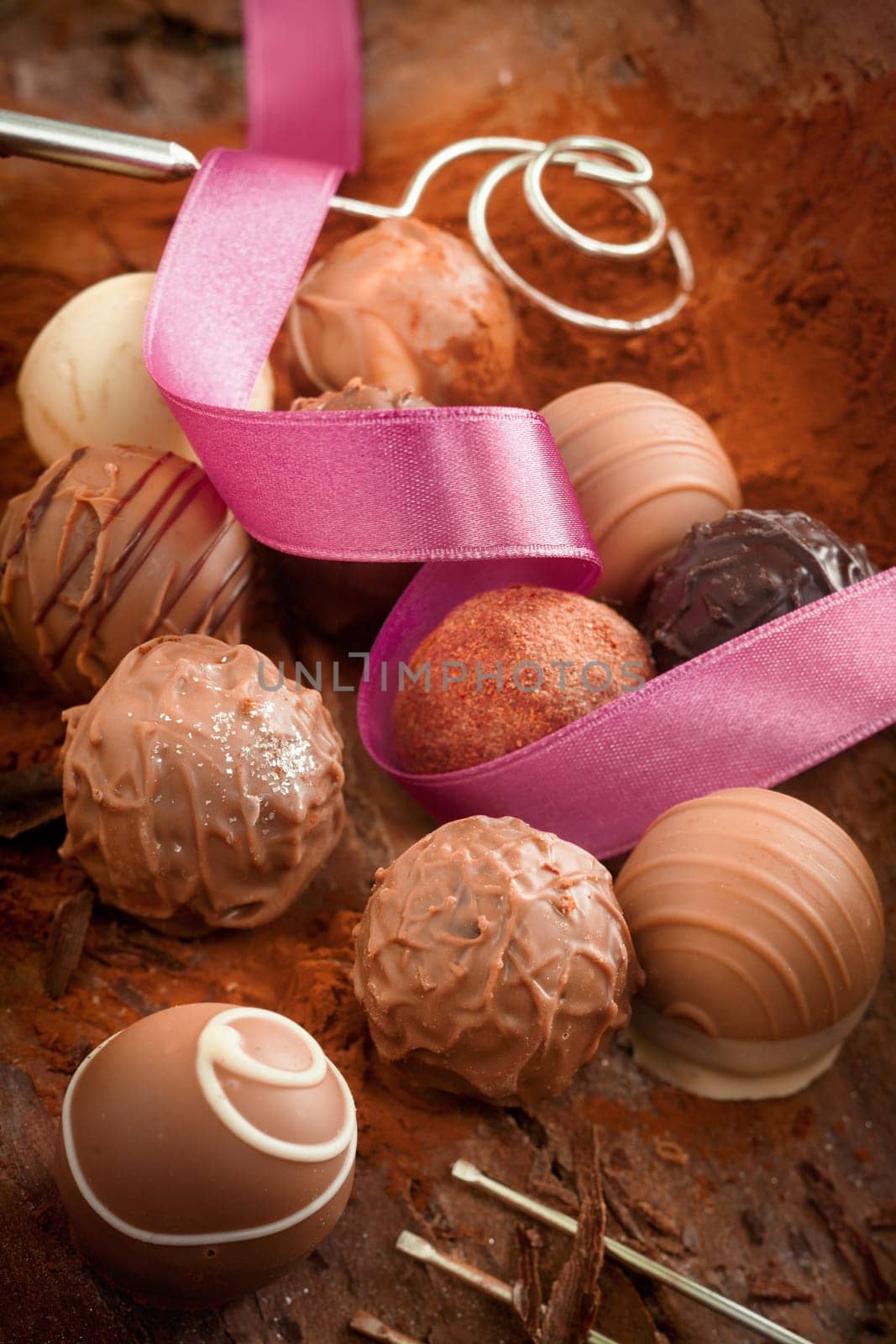 Decorative luxury handmade chocolates on a bed of cocoa powder with a spiralled pink ribbon for a celebration or gift