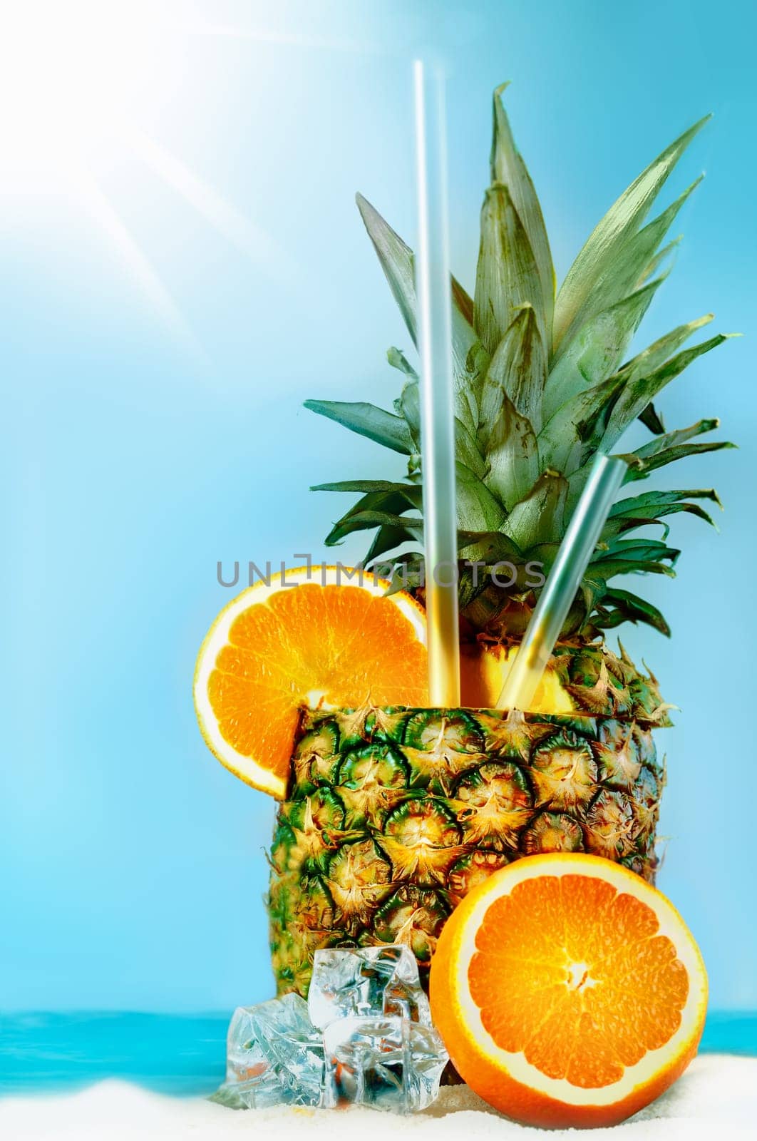 Pineapple with oranges and tubules on white beach sand. Fresh cold drink