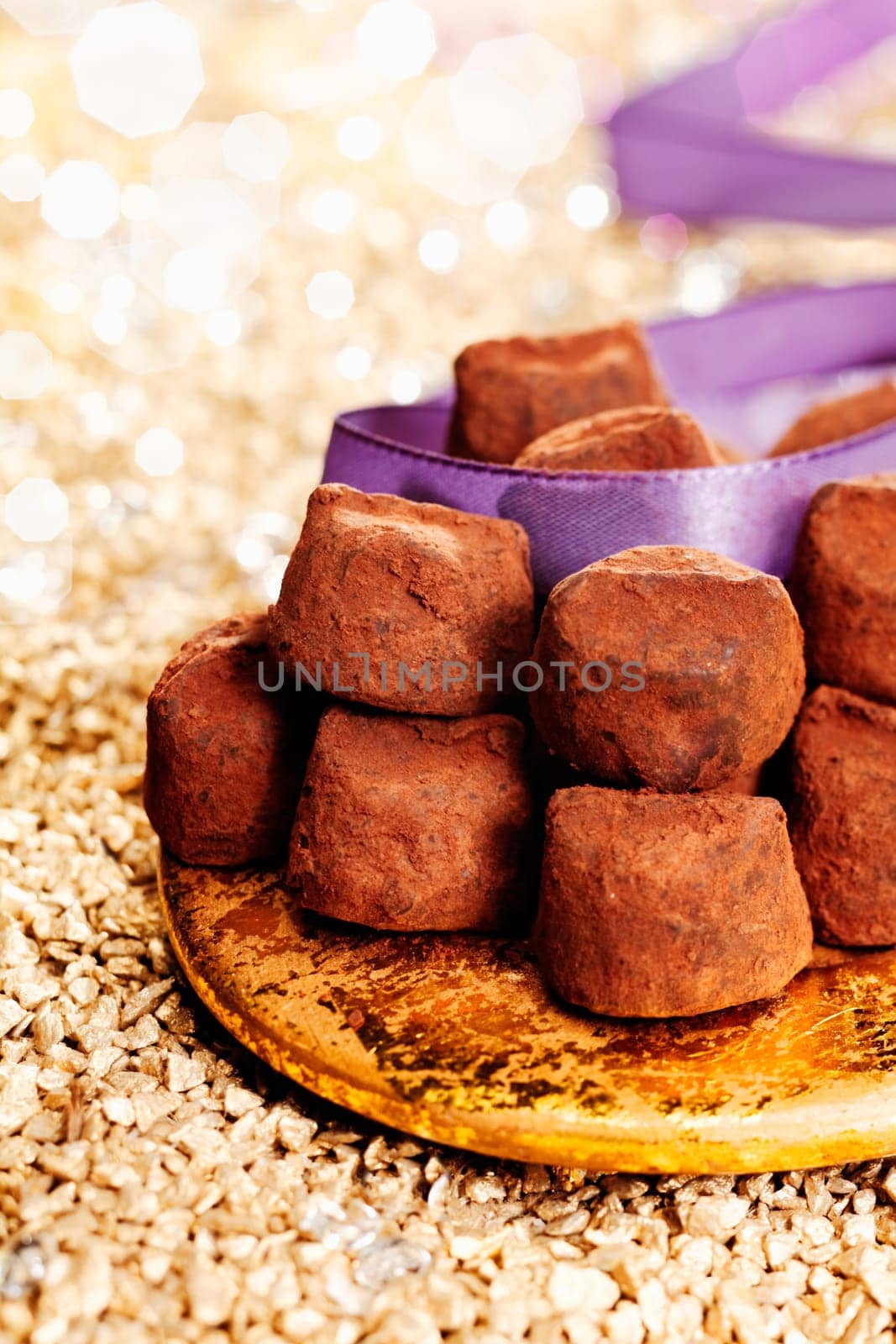 Plate of luxury handmade chocolate confectionery with a purple ribbon and background bokeh of twinkling party lights