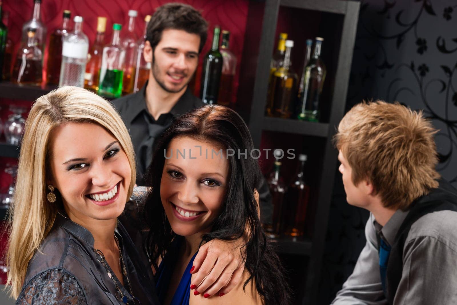Young happy girl friends at cocktail bar hugging together