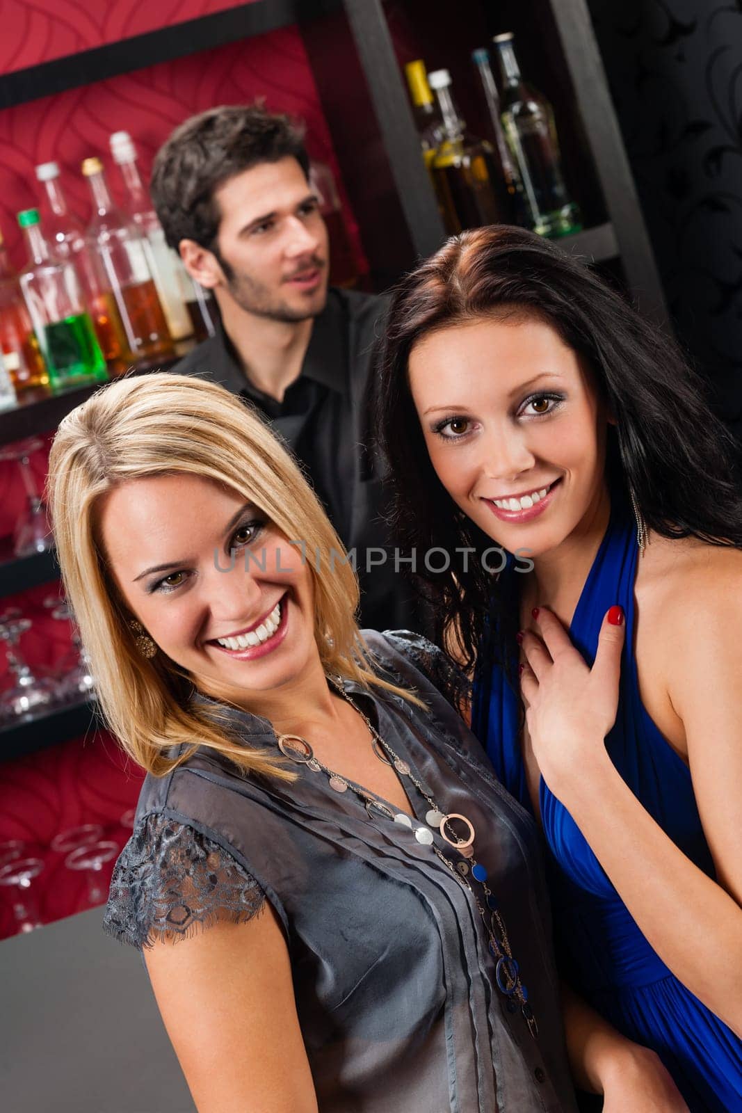 Young happy girl friends at cocktail bar hugging together