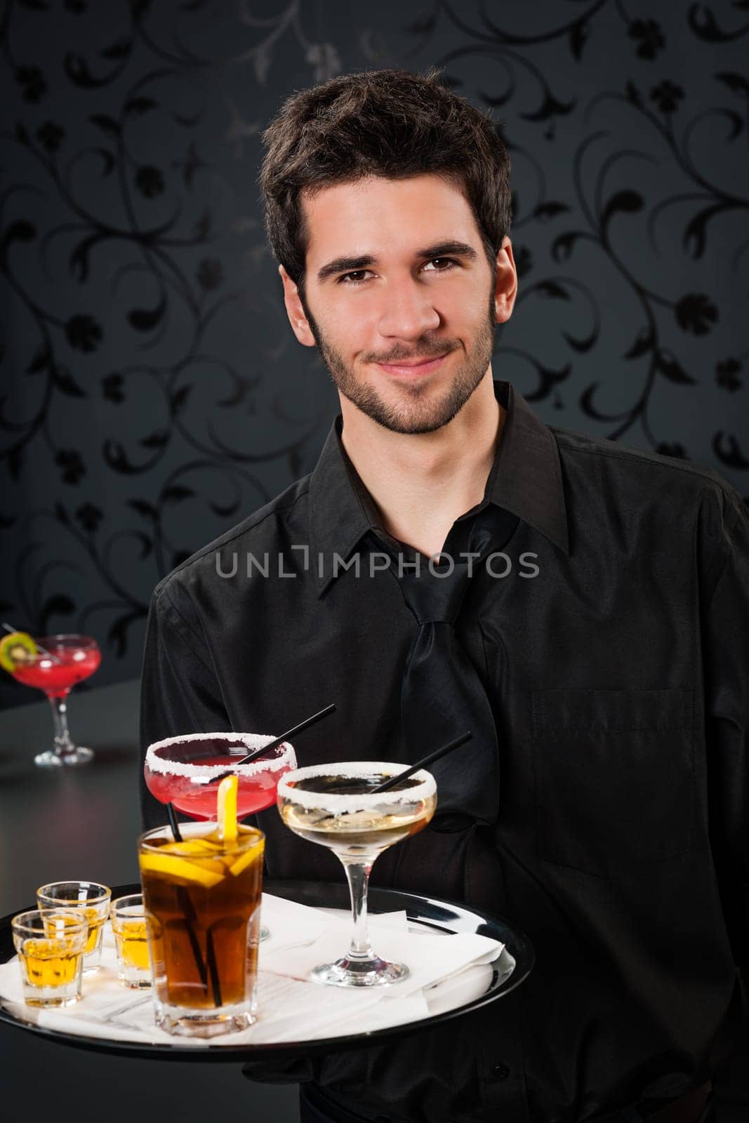 Portrait of handsome barman at bar holding tray with cocktails